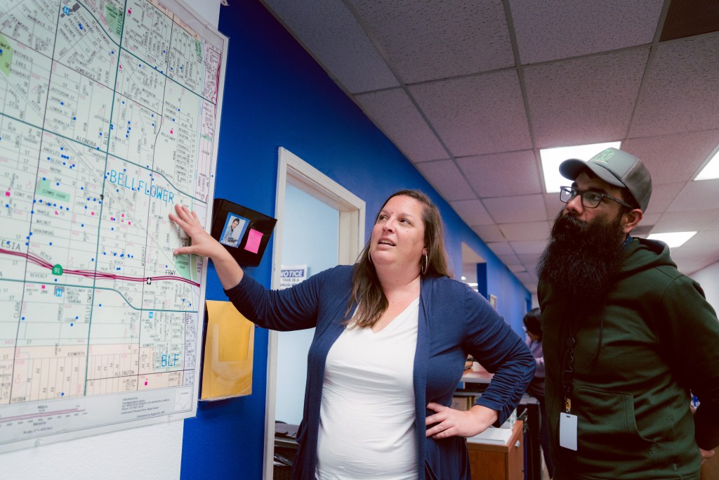 Two people look at a large map on a blue wall.