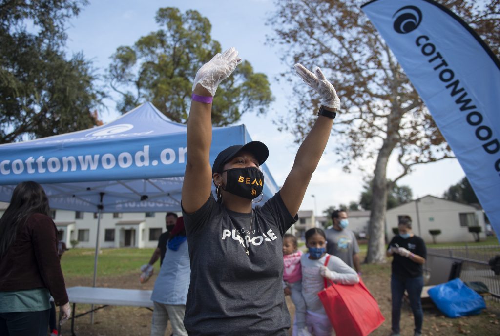 Person wearing gloves and mask raises arms near a tent.