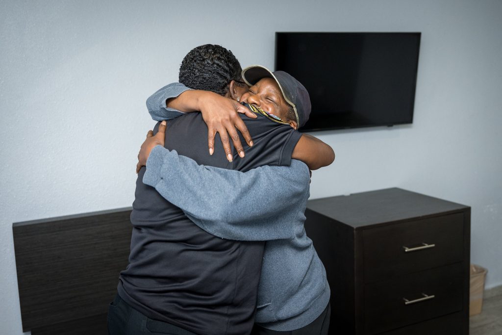 Two people embrace and smile indoors.