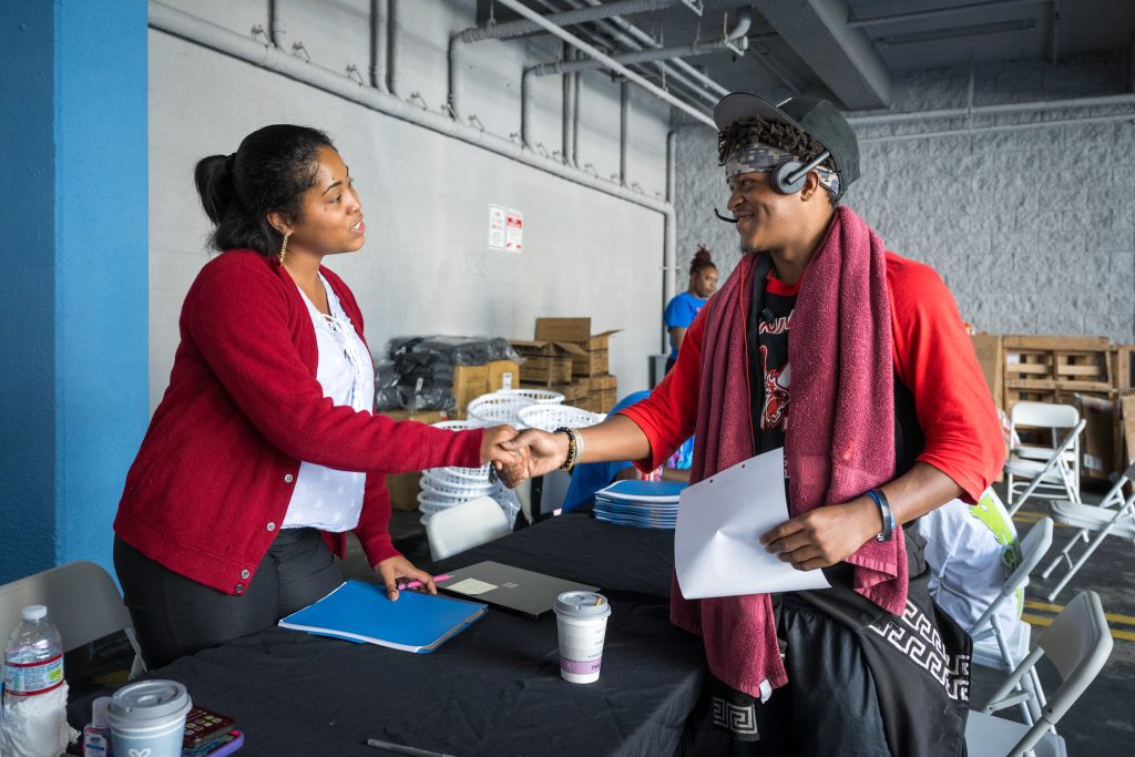 Two people shake hands at a table during what appears to be a community support or outreach event.