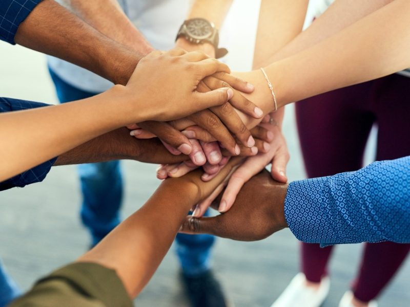 Multiple hands stacked together in a group gesture of unity and teamwork.