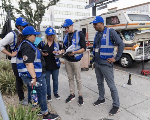 A team in blue safety vests gathers on a sidewalk, reviewing paperwork near RVs.