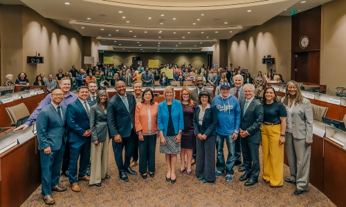 Team smiling in a large meeting room with an audience seated behind them.